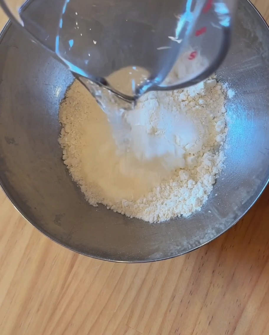 Primo piano di farina, acqua e lievito mescolati insieme in una ciotola di acciaio inossidabile per formare un impasto.