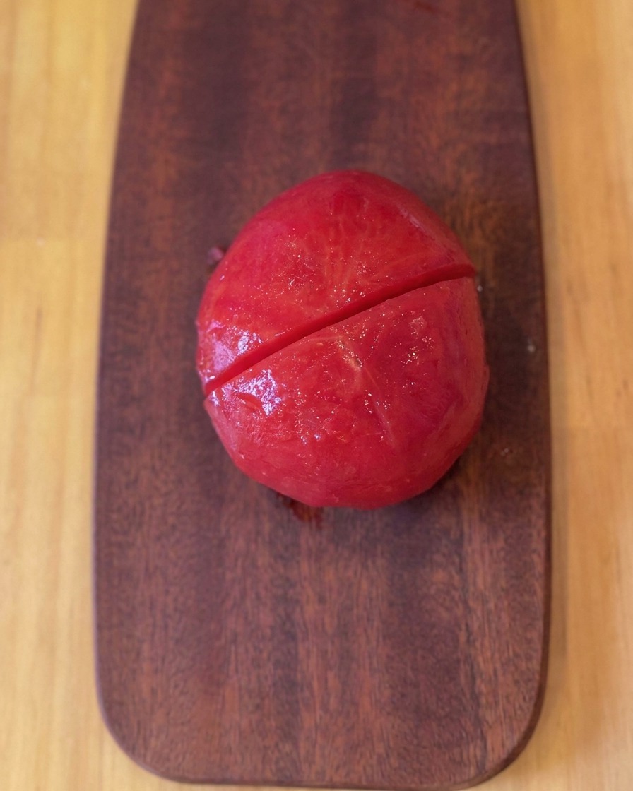 Un pomodoro sbucciato e abbrustolito su un tagliere di legno dopo essere stato tagliato a metà.