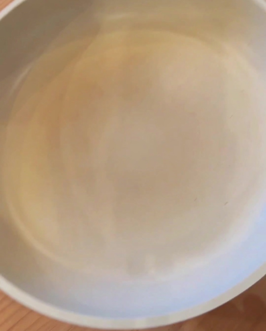 Un blocco di carne macinata che frigge in una padella con olio caldo, iniziando a dorarsi.
