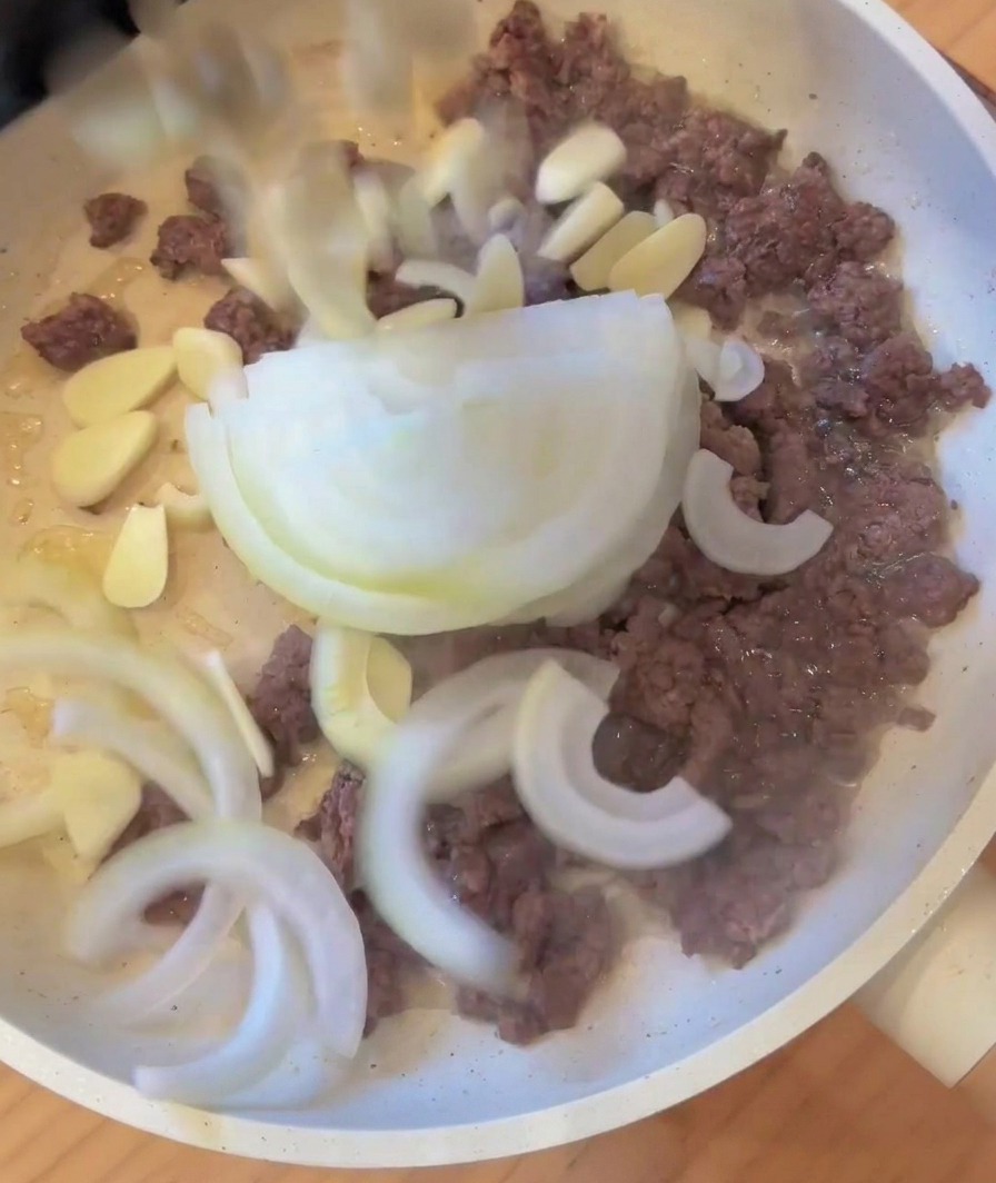 Cipolle a fette e aglio aggiunti a una padella con carne macinata rosolata.