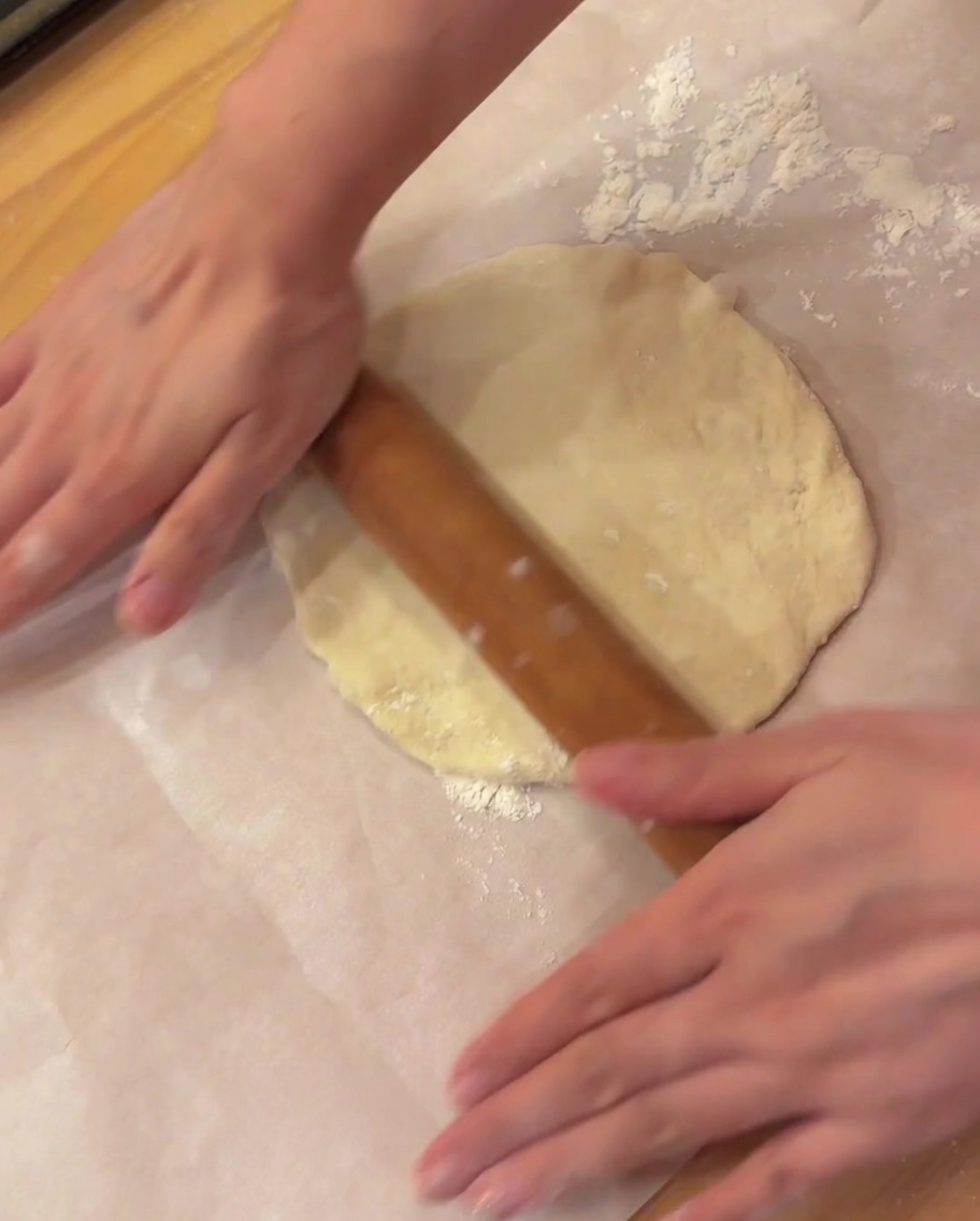 Un matterello di legno che appiattisce un pezzo rotondo di pasta per pizza su carta da forno.