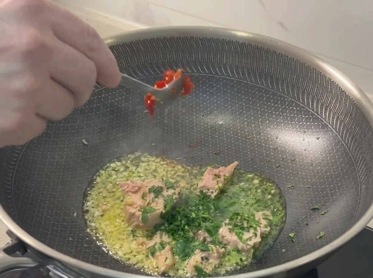 Un cucchiaio di metallo aggiunge del peperoncino tritato in padella.