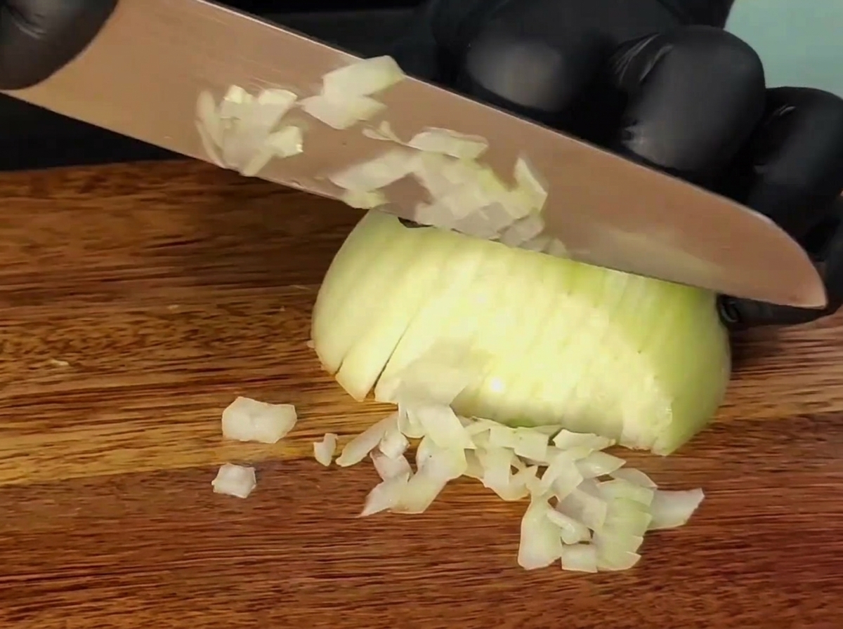 Un coltello che affetta una cipolla su un tagliere di legno.