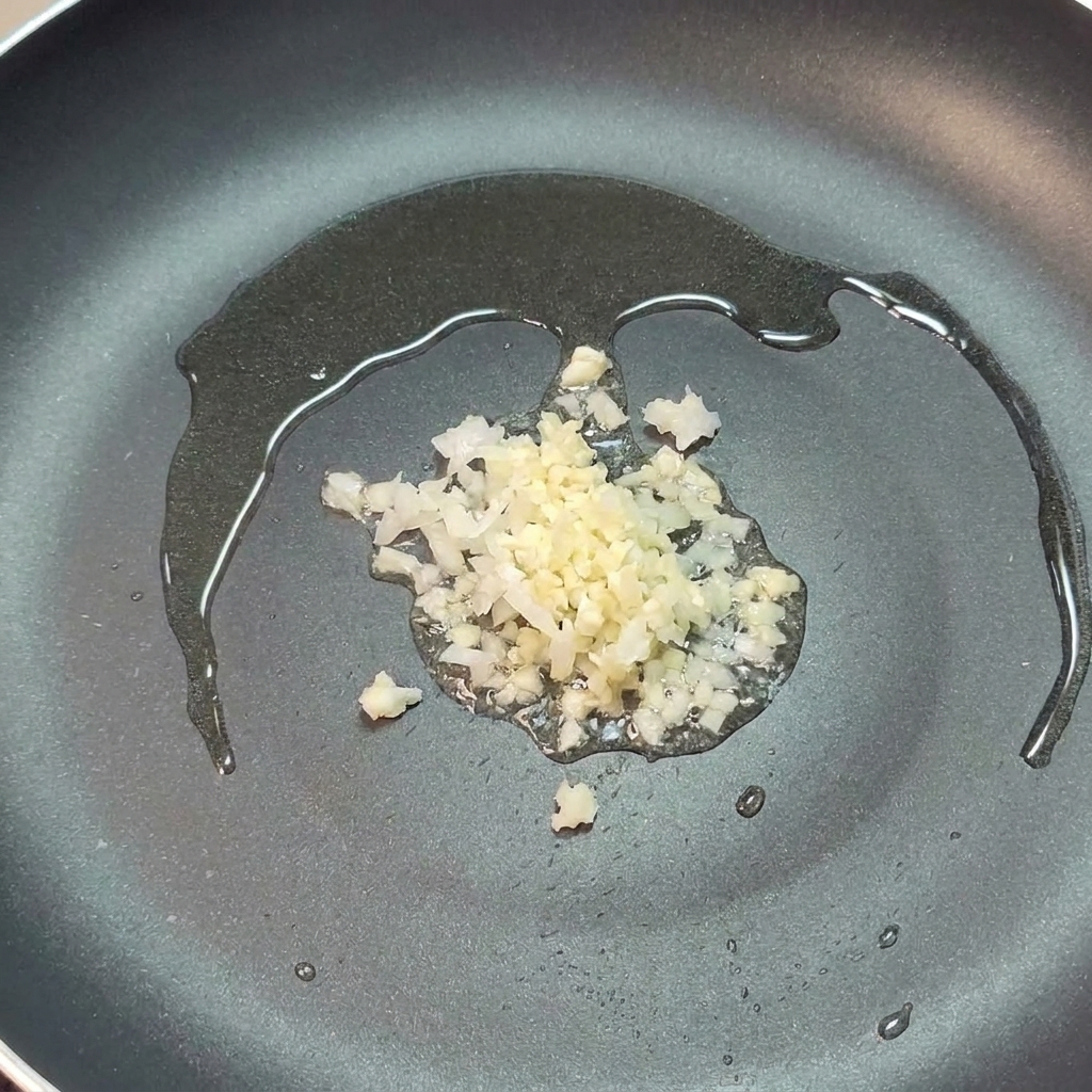 Cipolla tritata e aglio che sfrigolano nellolio doliva in una padella scura.