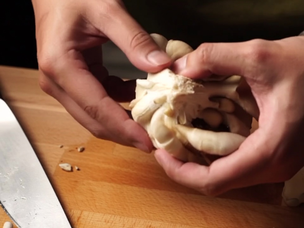 Mani che strappano funghi freschi in pezzi più piccoli.