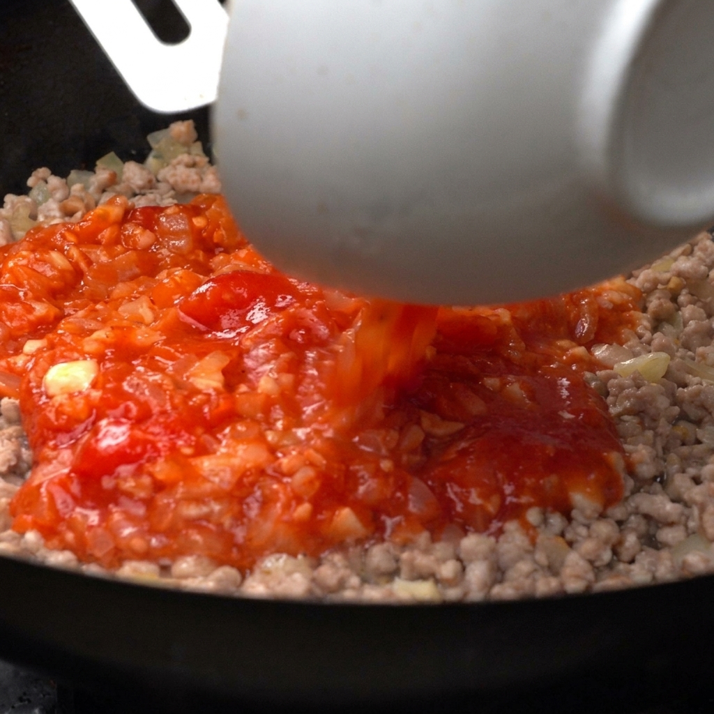Pomodori pelati versati in padella con la carne.