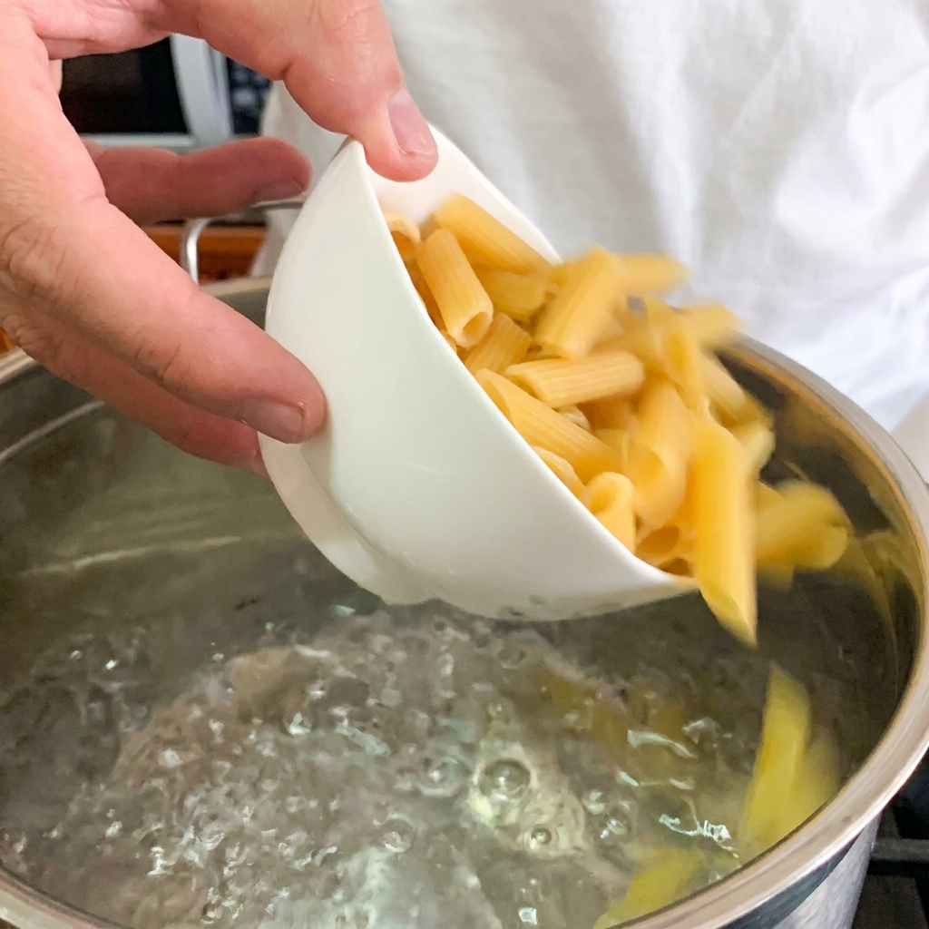 Un primo piano di un uovo in camicia posizionato al centro di una ciotola di penne cremose.