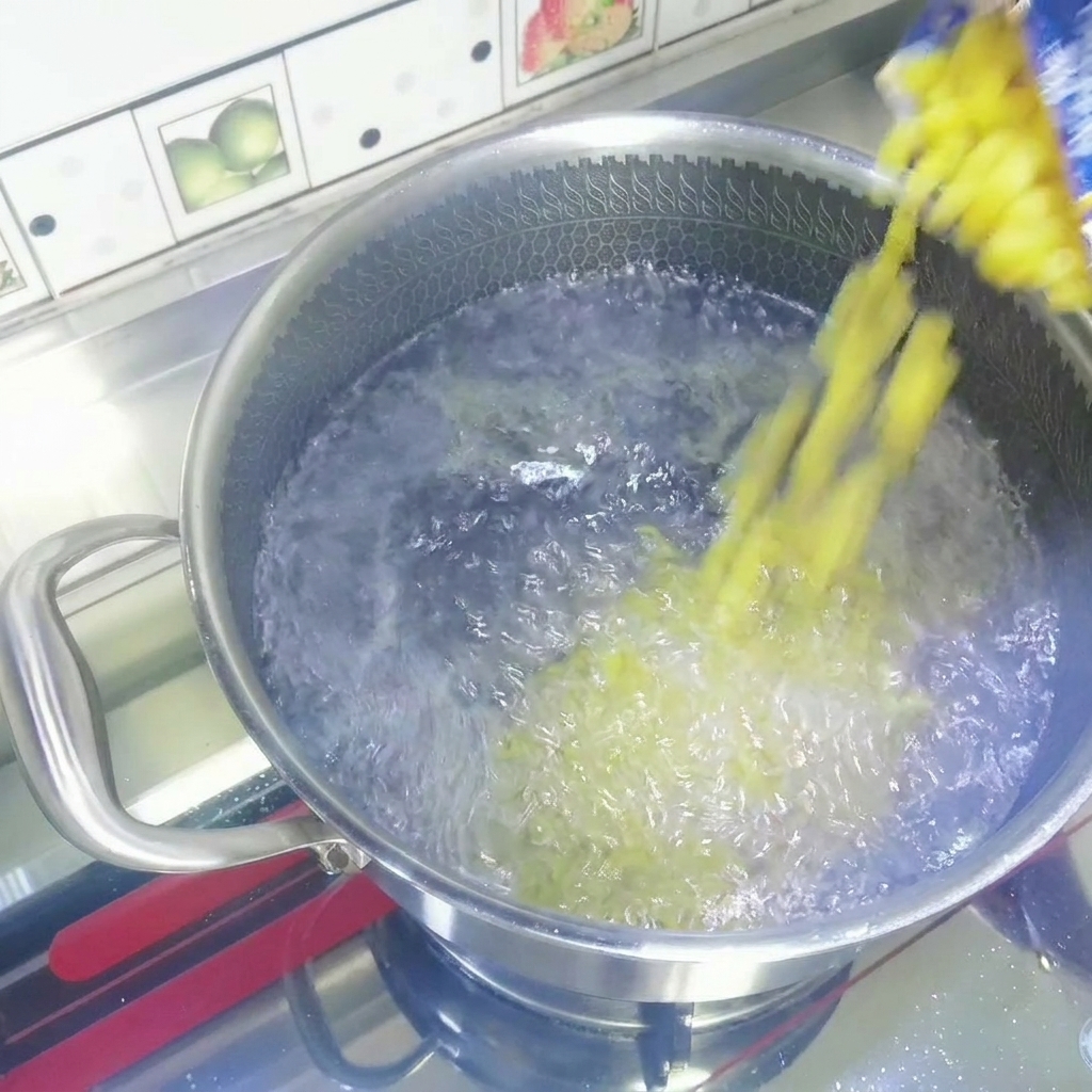 Maccheroni secchi gialli versati da un sacchetto in una pentola di acciaio inossidabile con acqua in ebollizione.