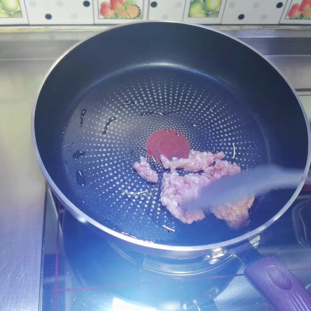 Carne macinata cruda saltata in una padella antiaderente scura riscaldata usando una spatola in silicone grigia.