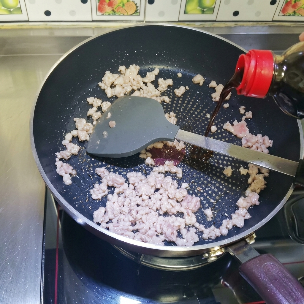 Salsa di soia liquida e scura versata da una bottiglia sulla carne macinata rosolata in una padella antiaderente.