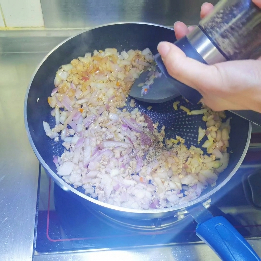 Pepe nero macinato fresco da un mulinello in una padella contenente carne macinata in rosolatura e cipolle a cubetti.