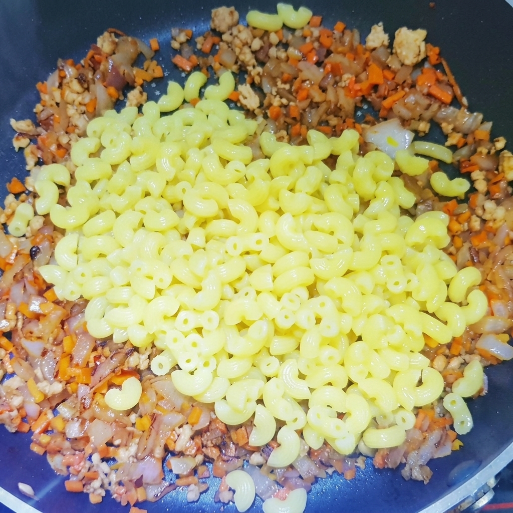 Maccheroni bolliti aggiunti a una padella piena di una base cotta di carne macinata, cipolle e carote.