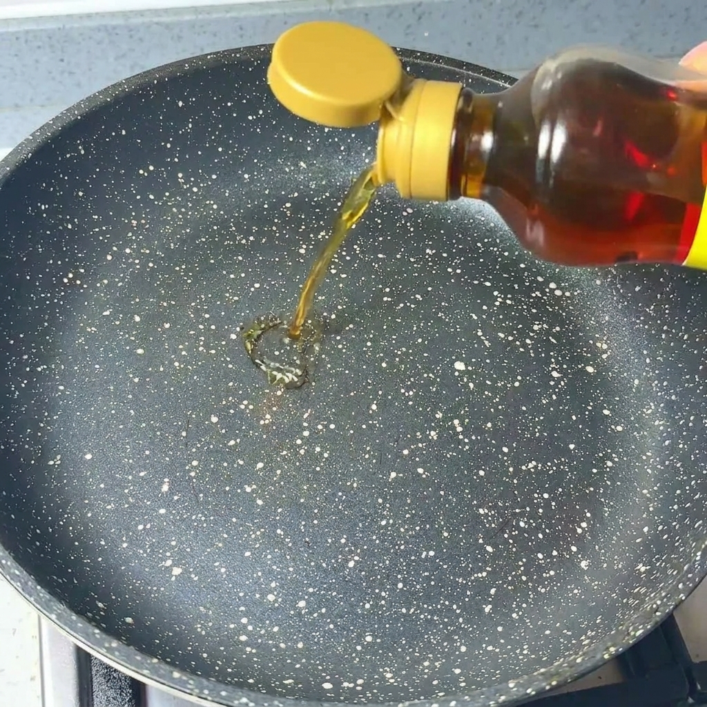 Olio di sesamo limpido versato da una bottiglia in una padella scura maculata.
