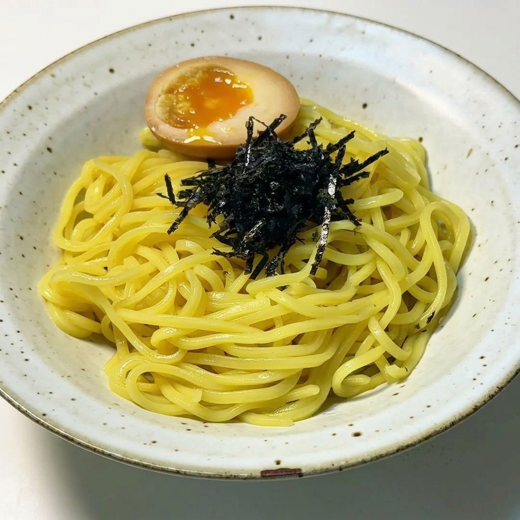 Noodle ramen impiattati e guarniti con un mucchietto di alga nera tritata e un uovo barzotto perfettamente diviso a metà, con un tuorlo arancione fondente.