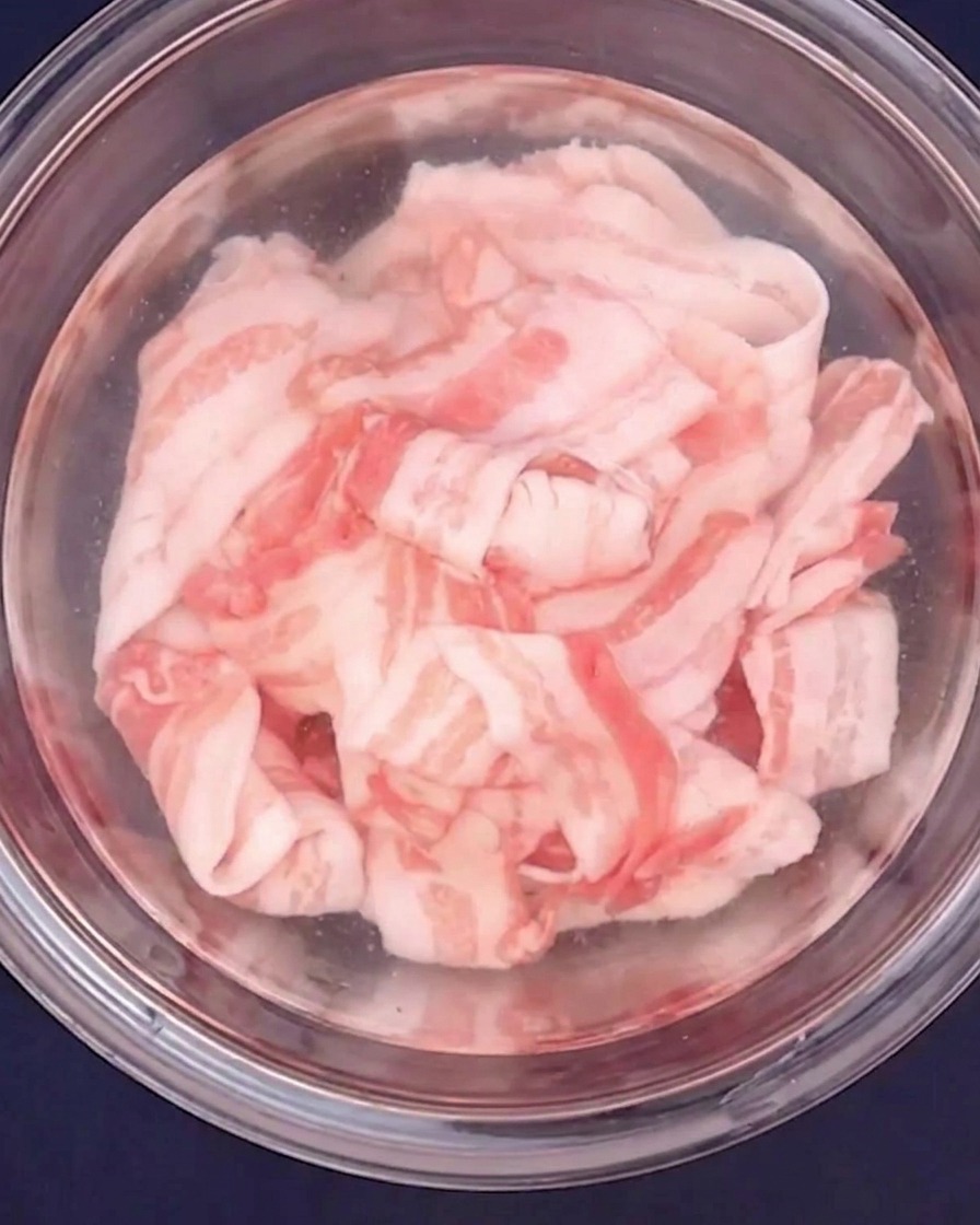 Pancetta affettata sottile che viene sbollentata in acqua calda in una ciotola di vetro.