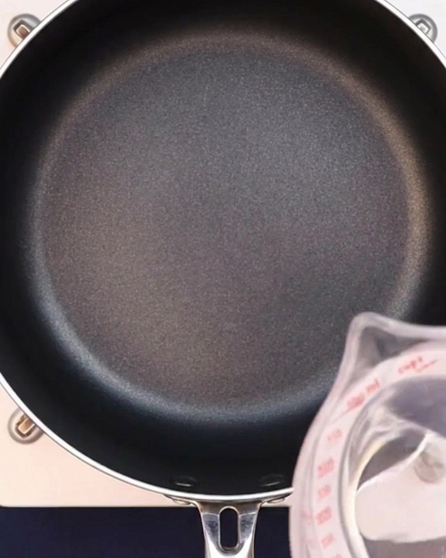 Acqua che viene versata in una padella nera per iniziare il brodo al curry.