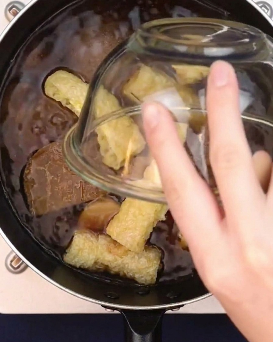 Tofu fritto a cubetti che viene aggiunto in una pentola di brodo al curry che sobbolle.
