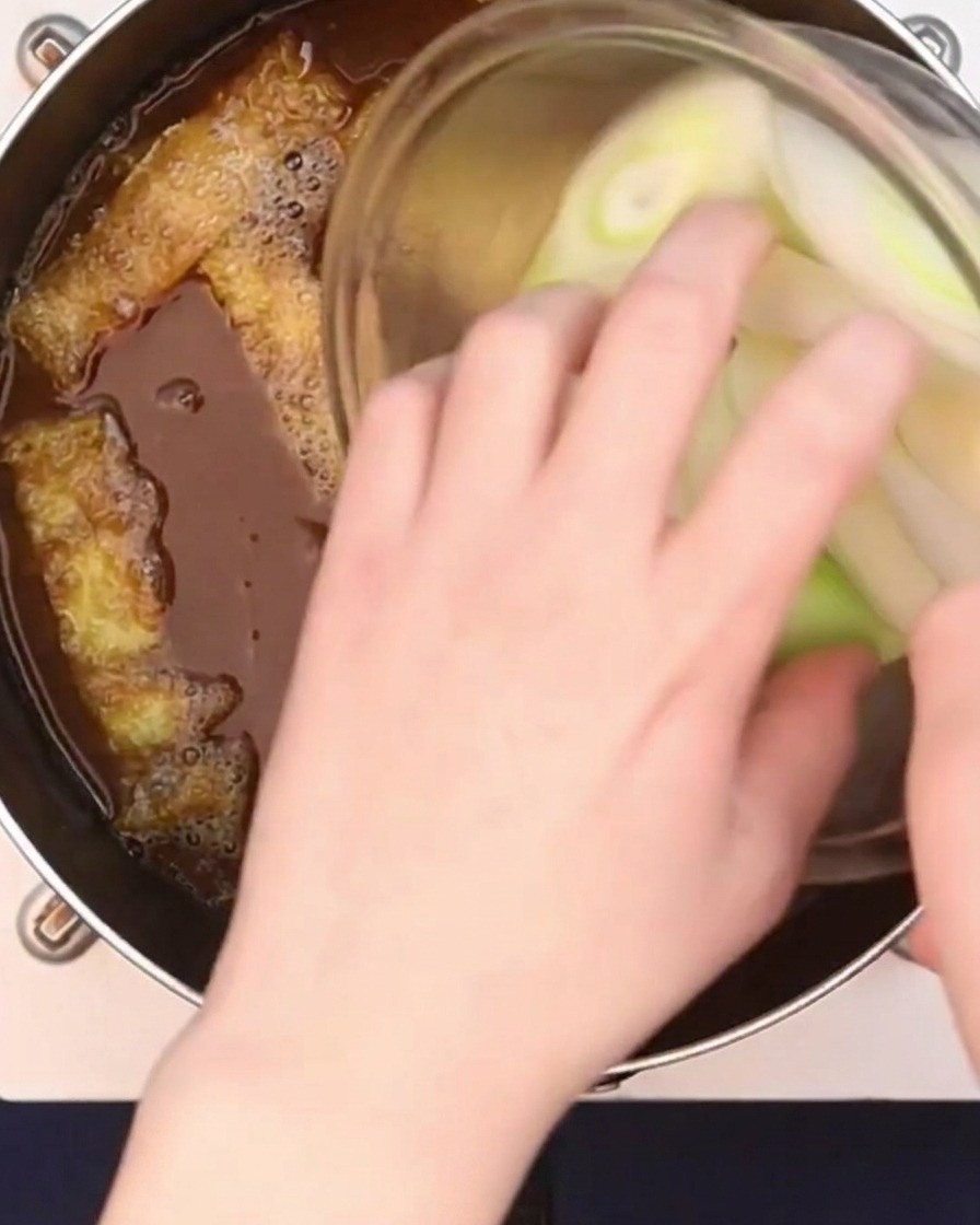 Cipollotti grandi tagliati diagonalmente che vengono aggiunti al brodo al curry che sobbolle.