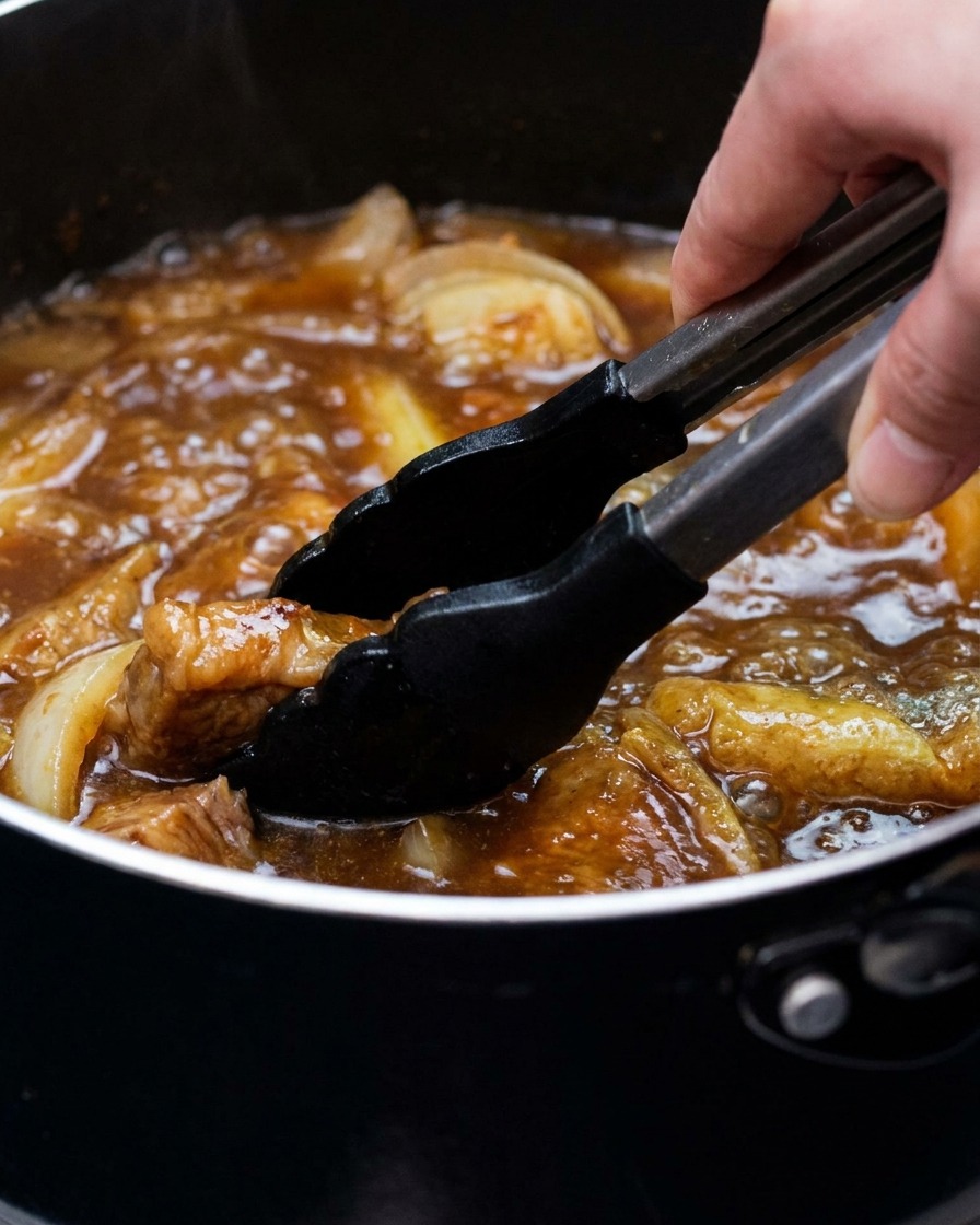 Una pentola di brodo al curry con tofu e cipollotti mescolata con delle pinze.