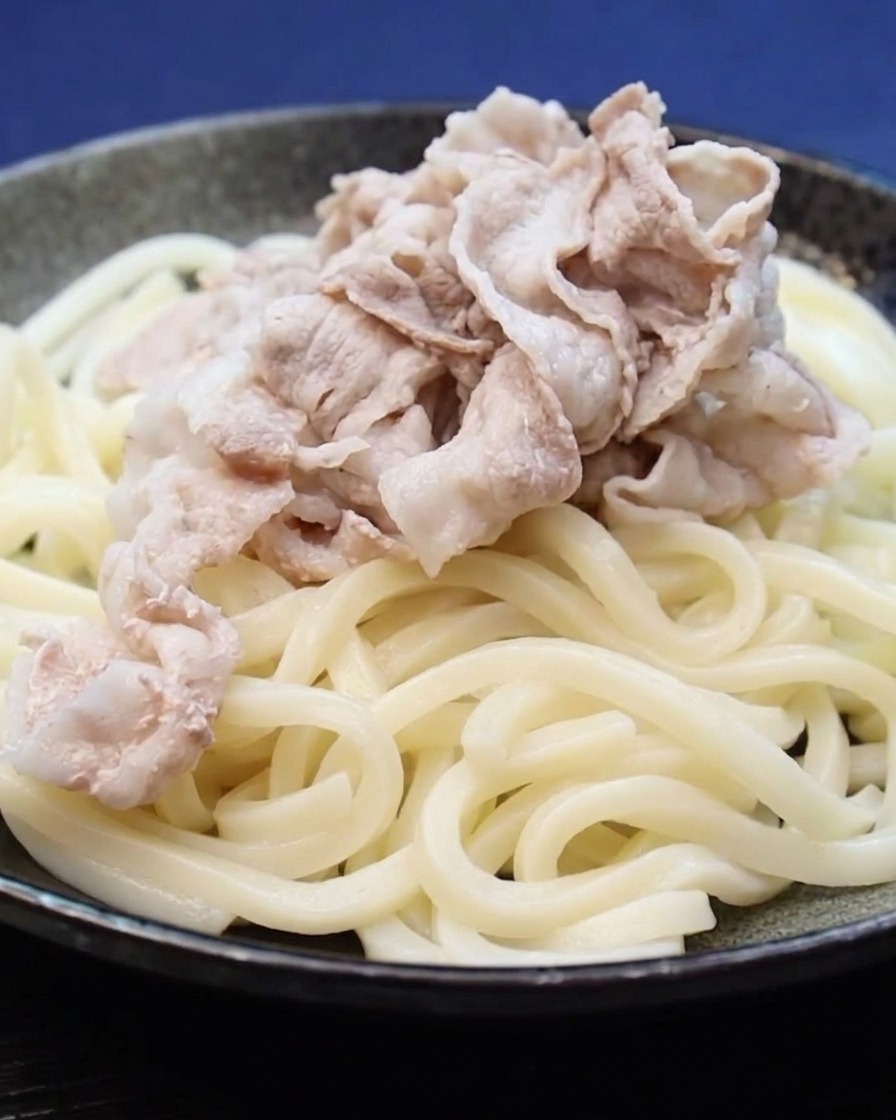 Fette di pancetta di maiale cotta posizionate su un letto di noodles udon.