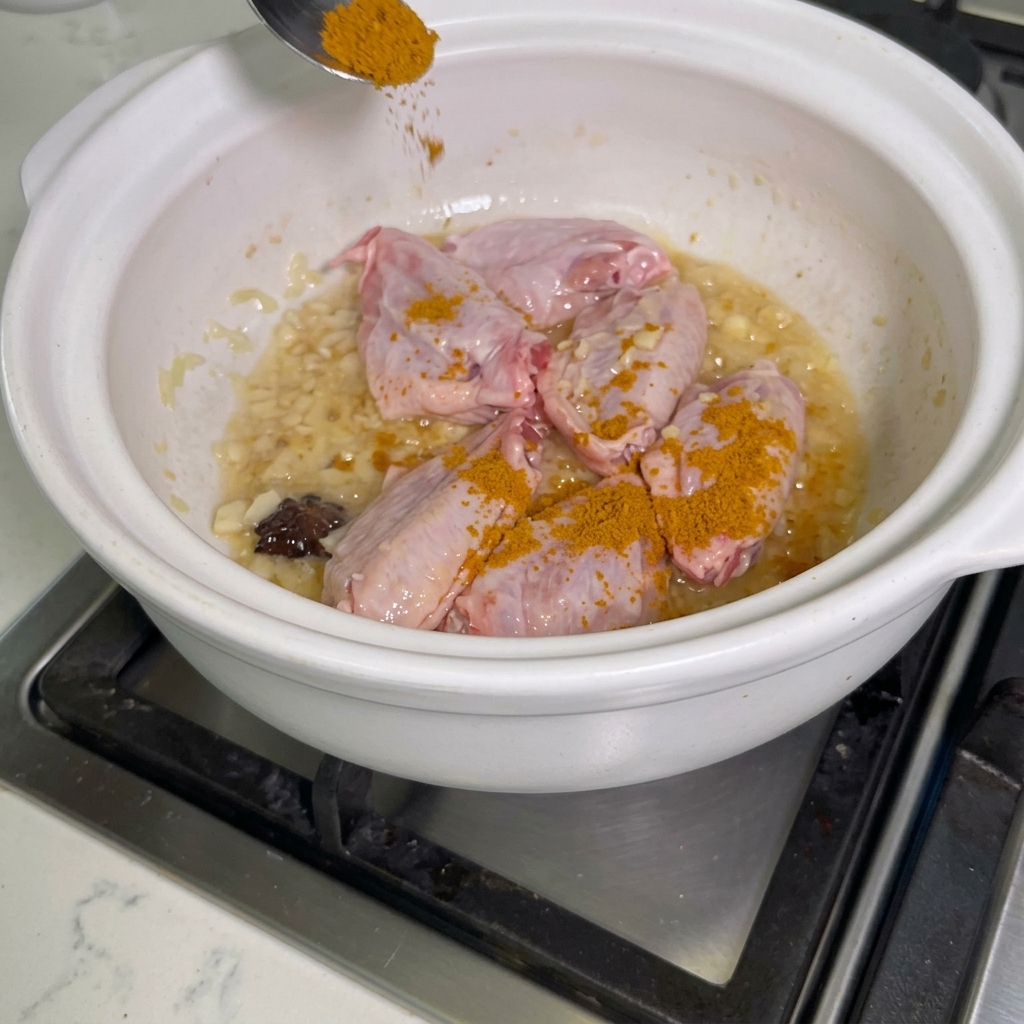 Curry in polvere cosparso sulle ali di pollo in una pentola.