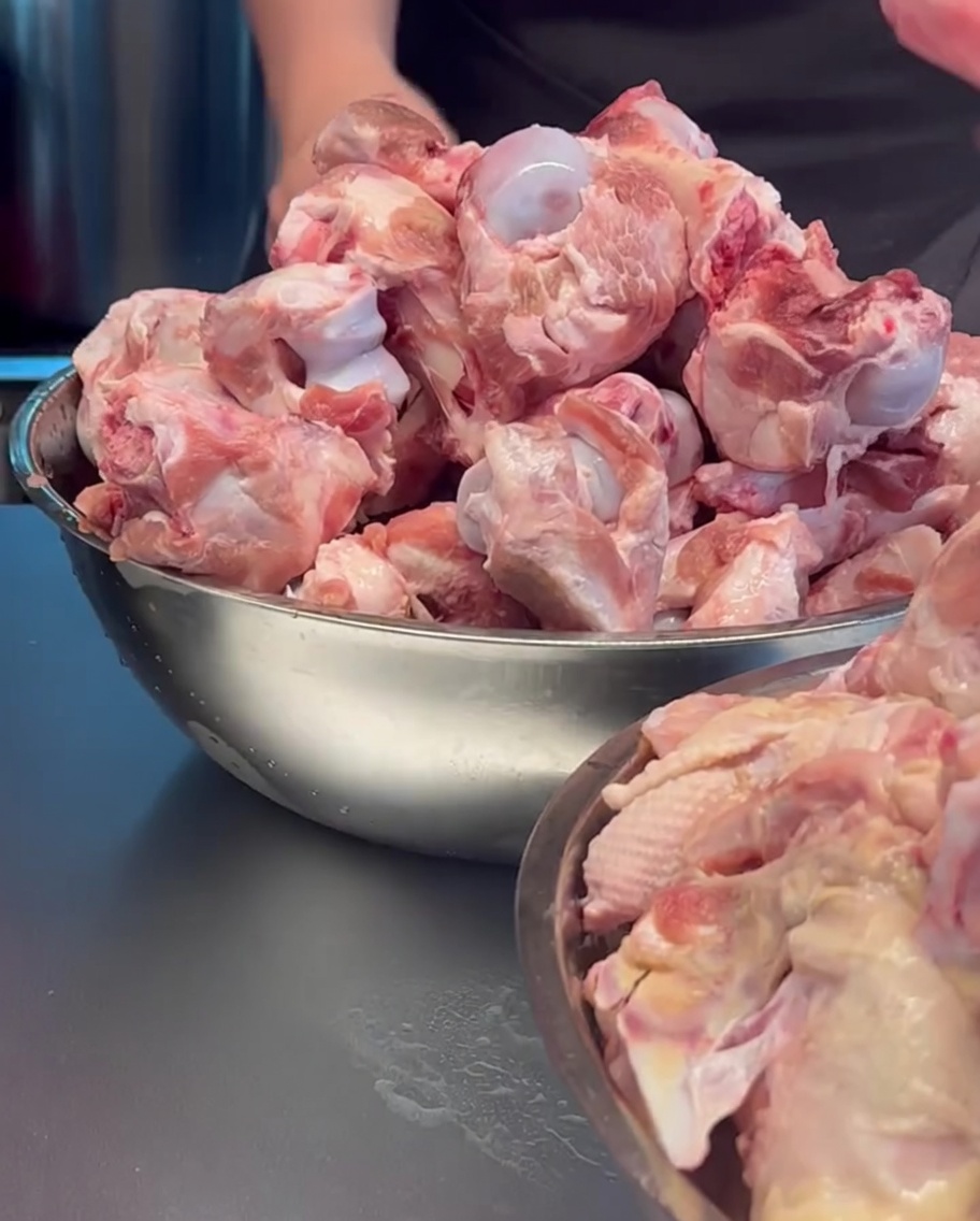 Ossa di maiale crude e carcasse di pollo inserite in una grande pentola di metallo.