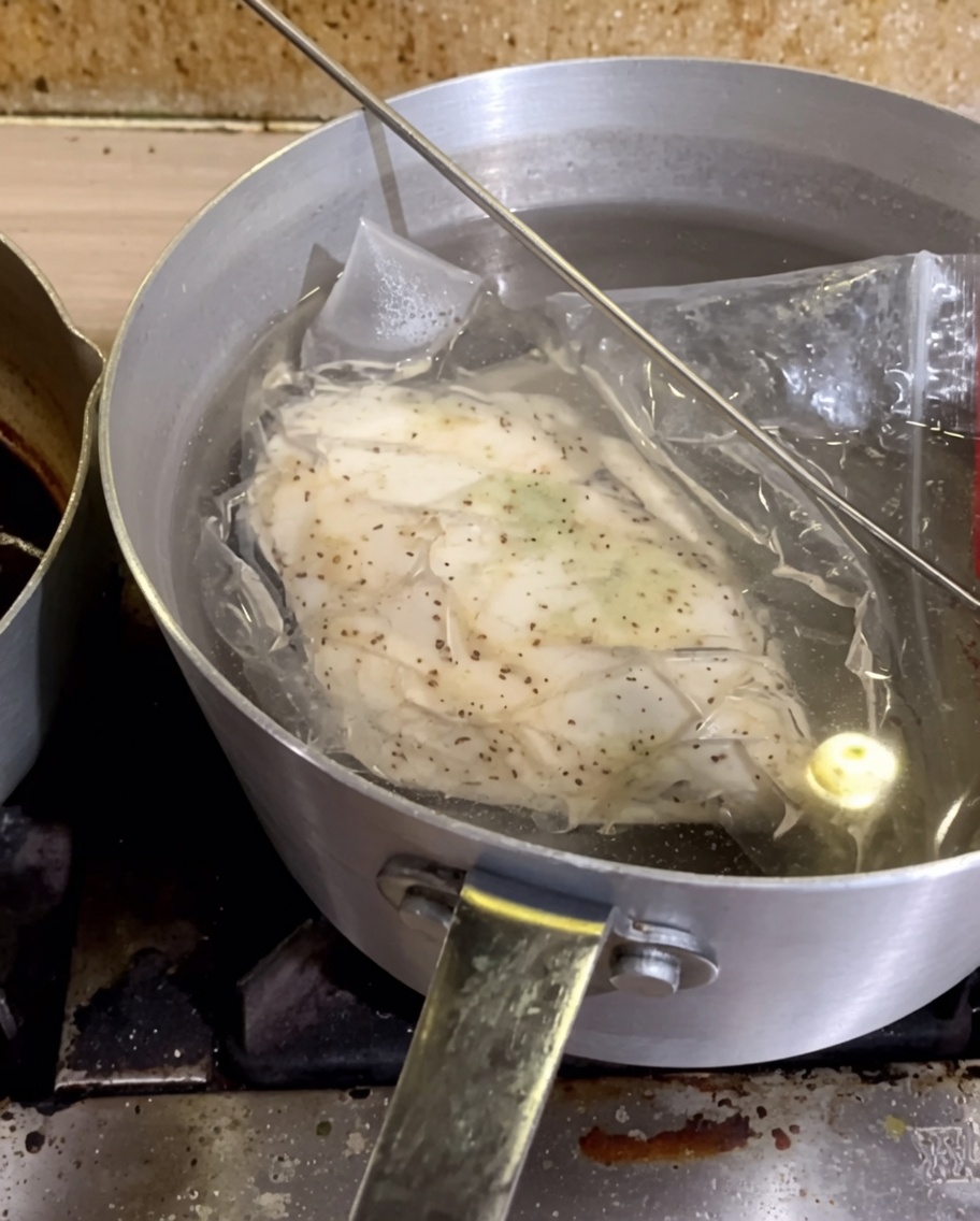 Un sacchetto sottovuoto contenente il petto di pollo condito immerso in una pentola dacqua calda.