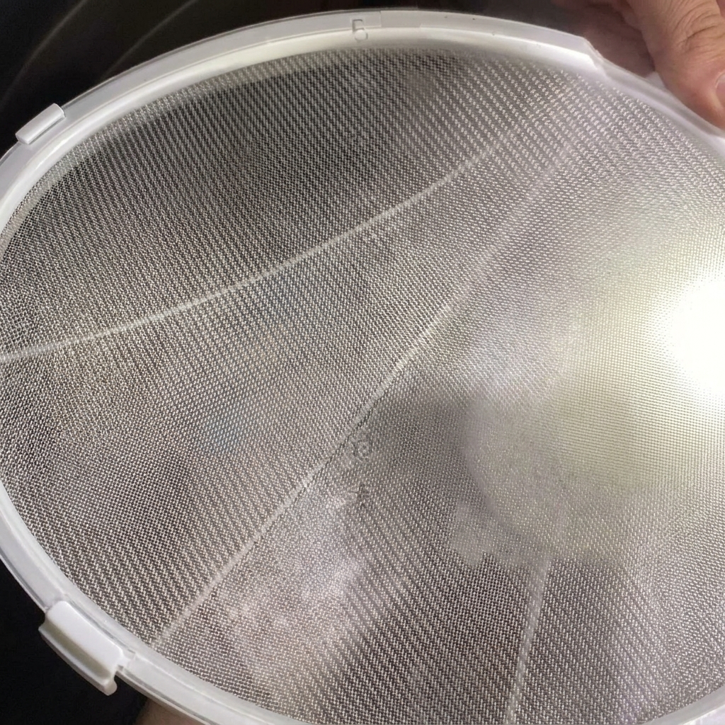 Un colino a maglie fini tenuto sopra una pentola mentre viene versato il brodo di pollo bianco e cremoso.
