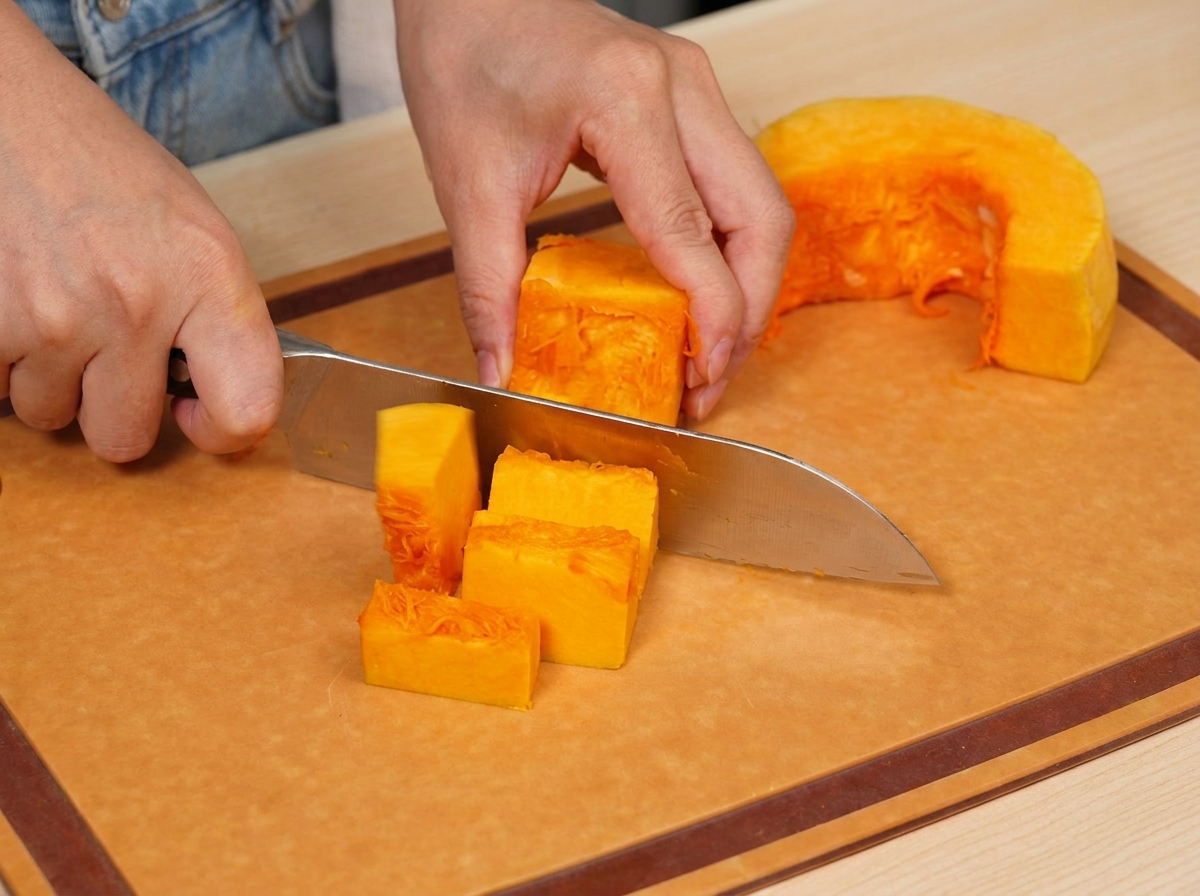 Zucca fresca arancione tagliata a cubetti uniformi su un tagliere di legno.