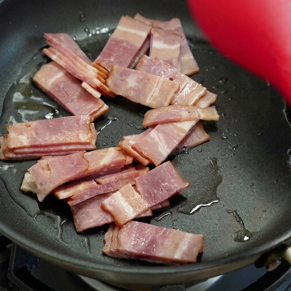 Fette di bacon che rosolano in una padella nera, mescolate con una spatola.