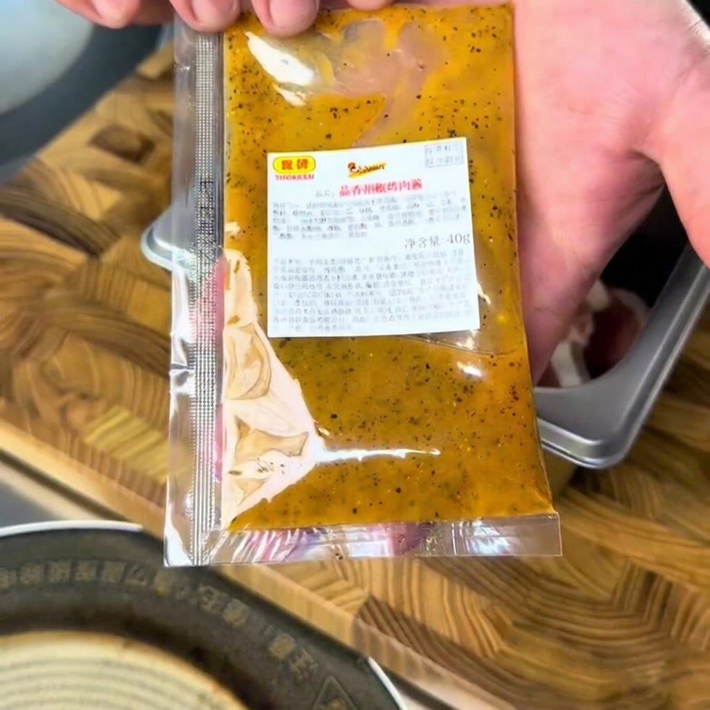 Salsa BBQ allaglio e pepe versata sulla carne cruda in un contenitore metallico.