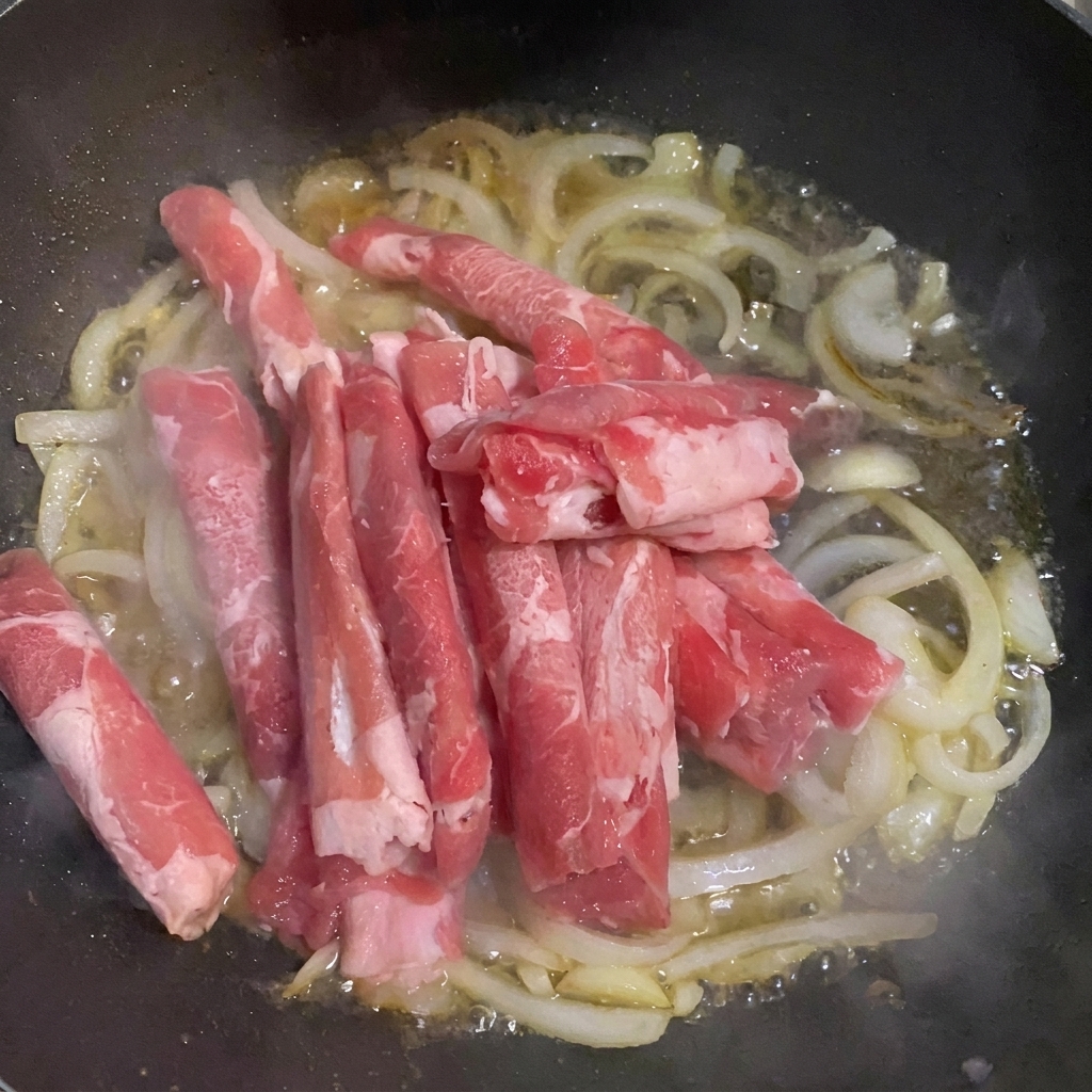 Sottili fette di manzo aggiunte alla padella con cipolle e acqua.