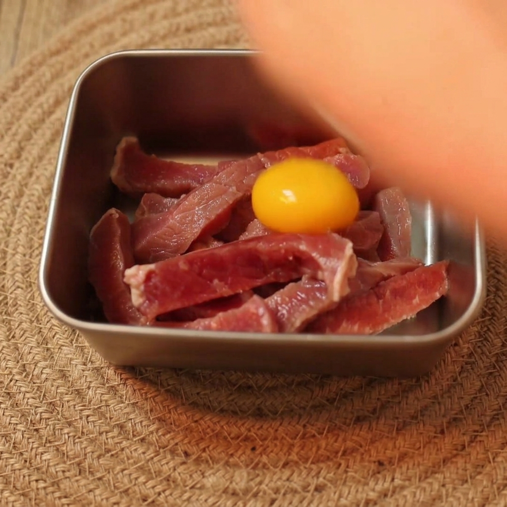 Un tuorlo duovo crudo giallo brillante sopra strisce di manzo crudo a fette in una ciotola di metallo.