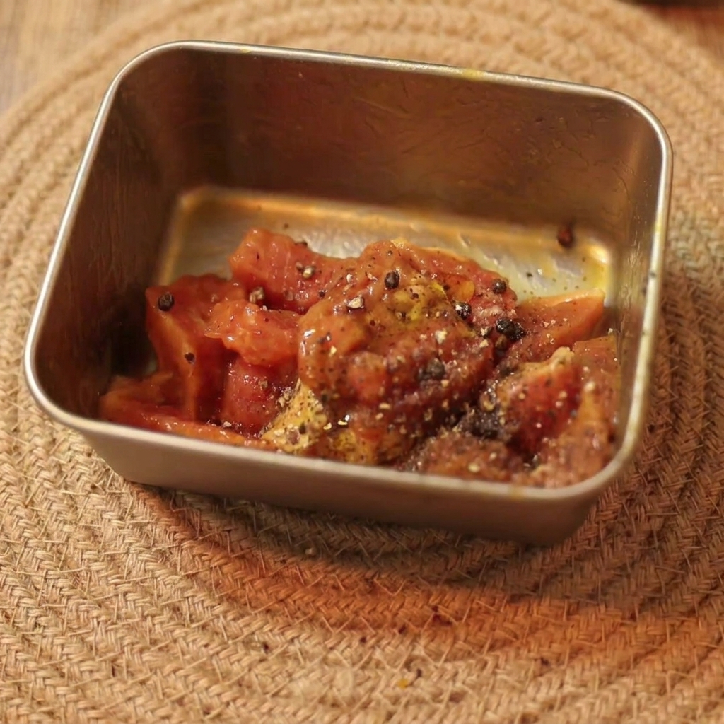 Manzo crudo a fette marinato e condito con pepe nero e olio in un piccolo contenitore rettangolare.