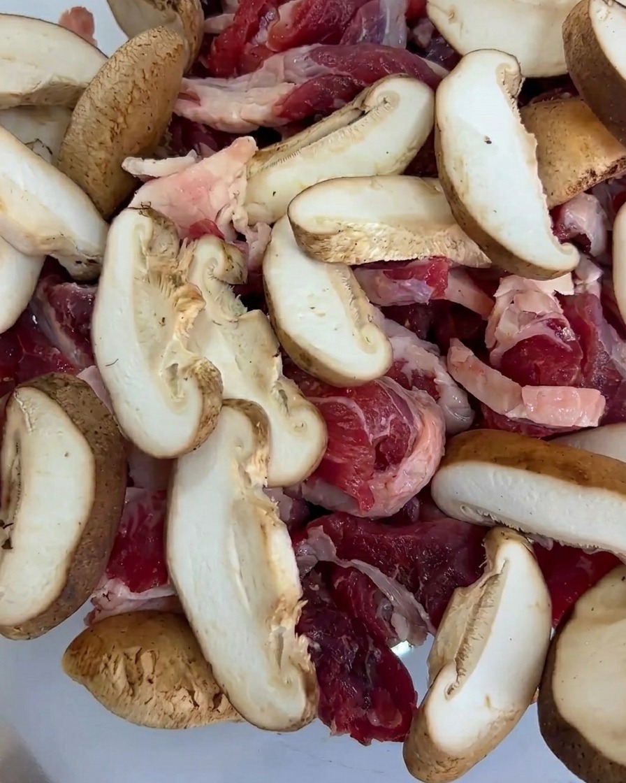 Pezzi di baby corn aggiunti alla teglia, mescolati con il manzo e le fettine di funghi.
