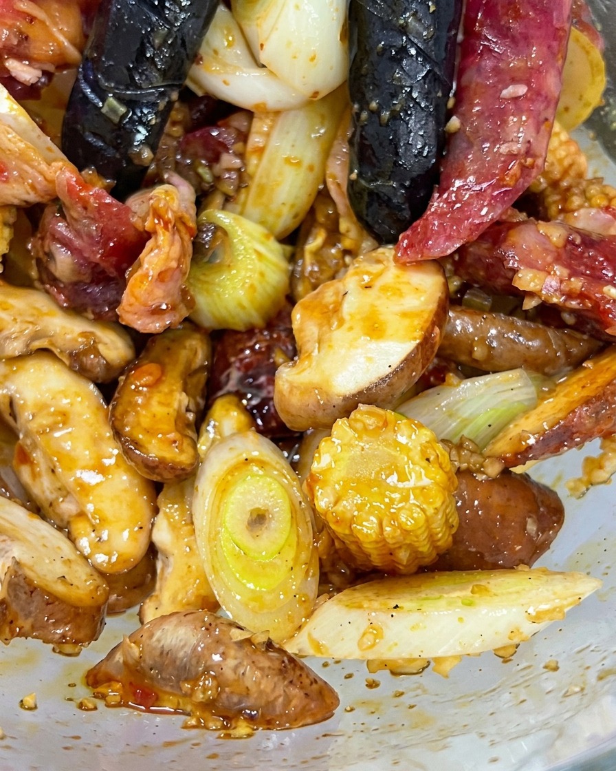 Mani con guanti che mescolano insieme manzo, funghi, baby corn e aromi in una ciotola di vetro.