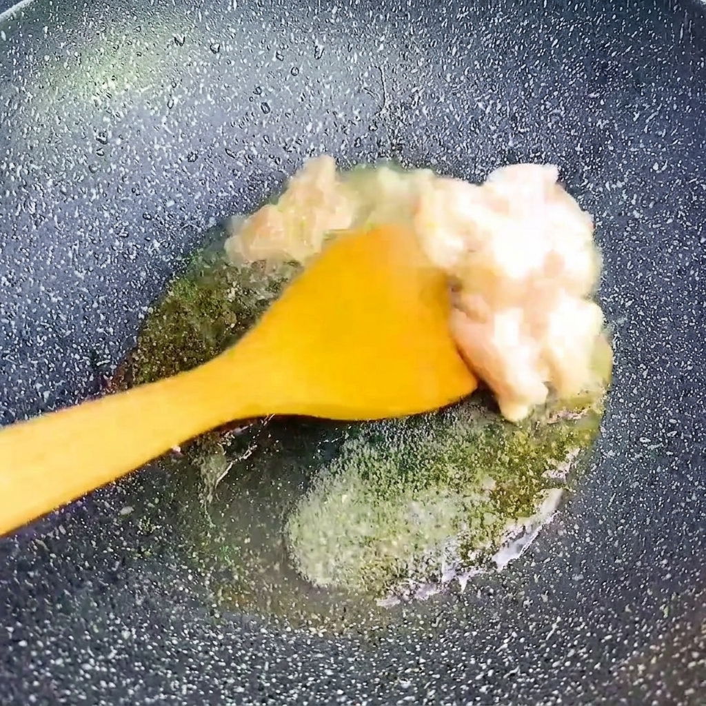 Piccoli cubetti di pancetta di maiale saltati con una spatola gialla in una padella scura e rovente.