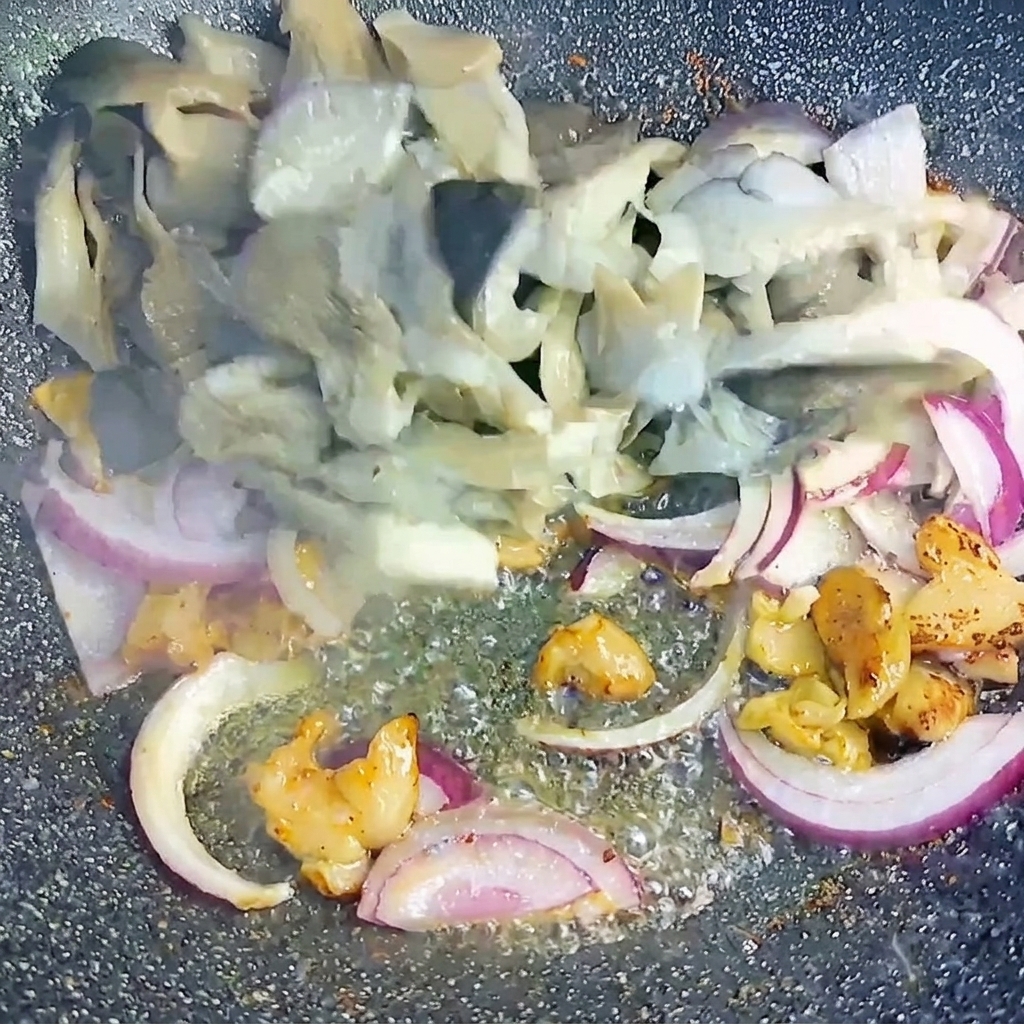 Funghi pleurotus sbollentati e cipolle rosse a fette saltati insieme ai pezzetti di pancetta rosolata nel wok.