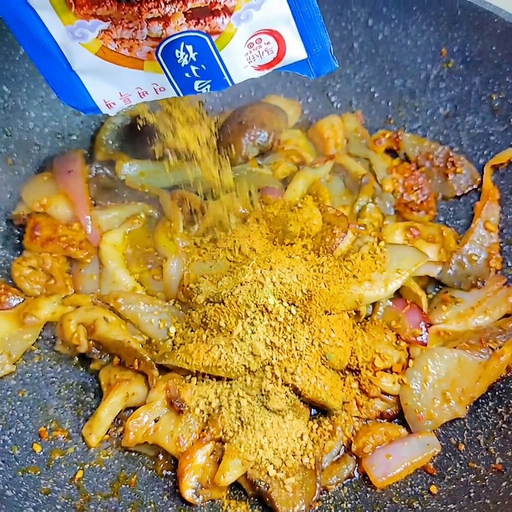 Una bustina blu che versa linsaporitore BBQ coreano in polvere sui funghi e le cipolle nel wok caldo.