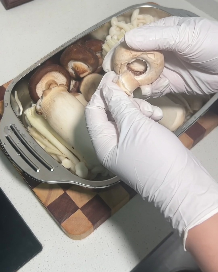 Una mano che rimuove il gambo da una cappella di fungo shiitake fresco e crudo.