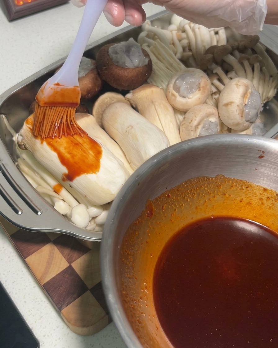 Salsa che viene spennellata sui funghi cardoncelli crudi allinterno di una teglia di metallo.
