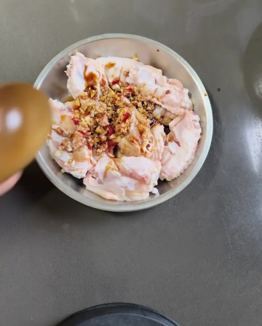 Alette di pollo crude in una ciotola di metallo mescolate con aglio, peperoncino, salsa di soia e olio di sesamo.