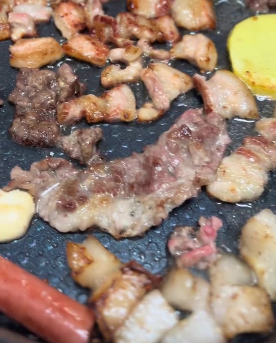 Pancetta di maiale, teste di funghi e fette di patate sfrigolanti su una griglia elettrica con una bella doratura.