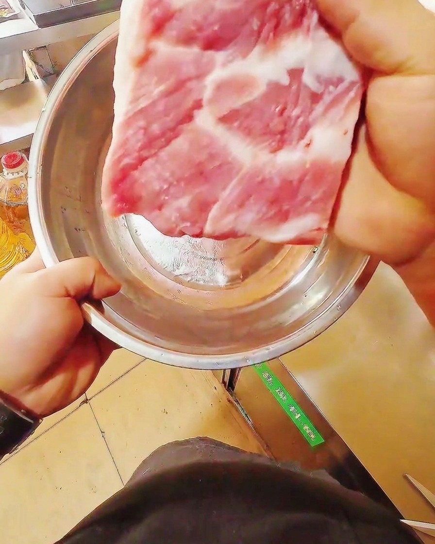 Un coltello affilato taglia un trancio di pancetta di maiale cruda su un tagliere di legno.