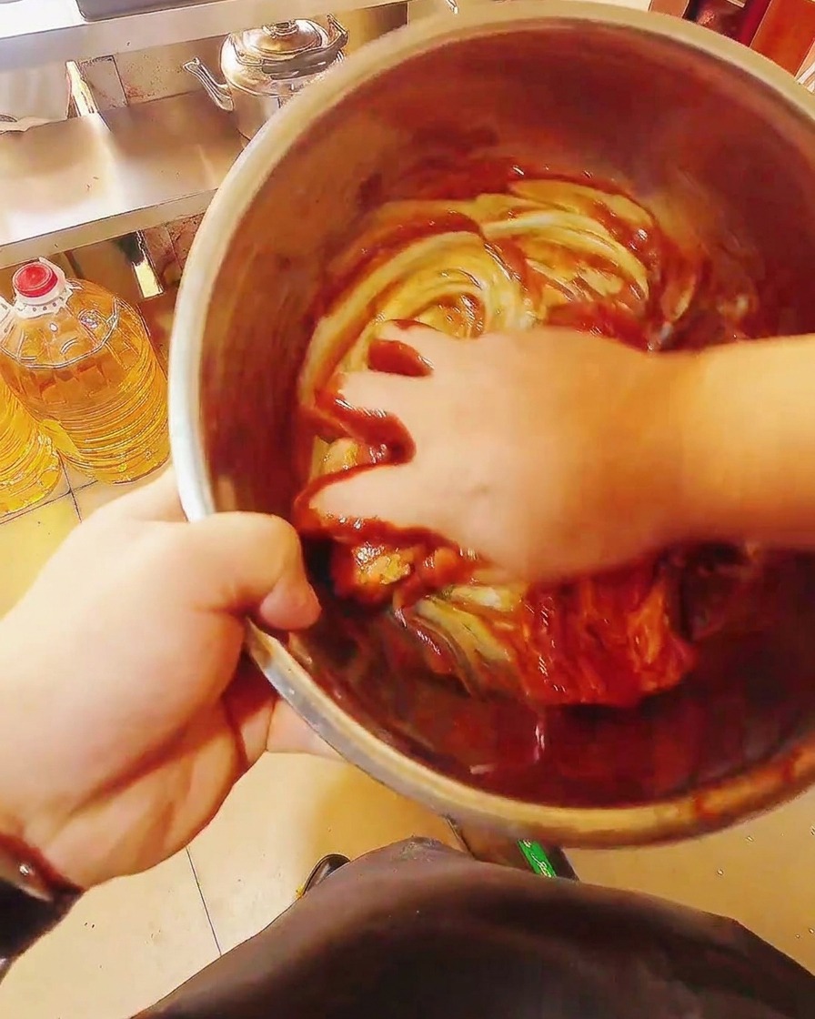 Strisce di pancetta cruda mescolate a mano in unampia ciotola con una marinatura densa e rossa.