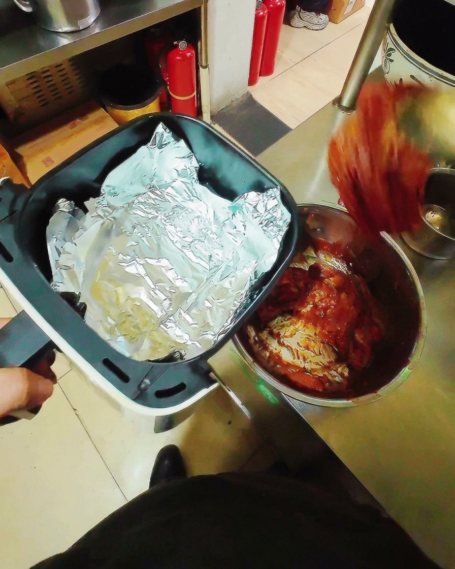 Strisce di maiale marinate adagiate in piano su carta stagnola allinterno del cestello di una friggitrice ad aria, pronte per la cottura.
