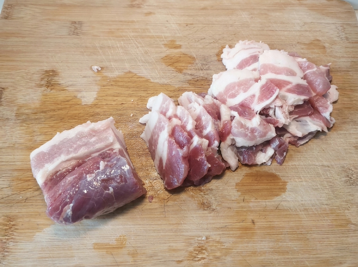 Sottili fette di pancetta di maiale cruda disposte ordinatamente su un tagliere di legno dopo essere state tagliate.