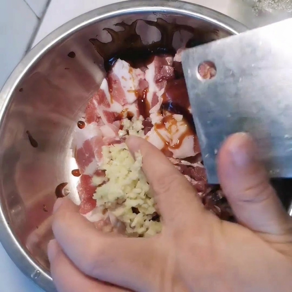 Una ciotola di metallo contenente la pancetta affettata, condita con aglio tritato e varie salse.