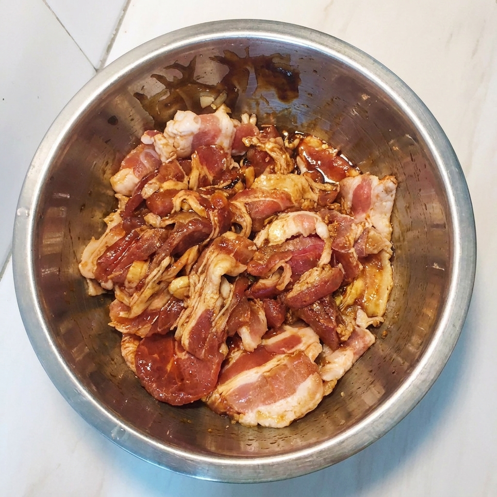 Fette di pancetta marinata mescolate in una ciotola di metallo per garantire una copertura uniforme.