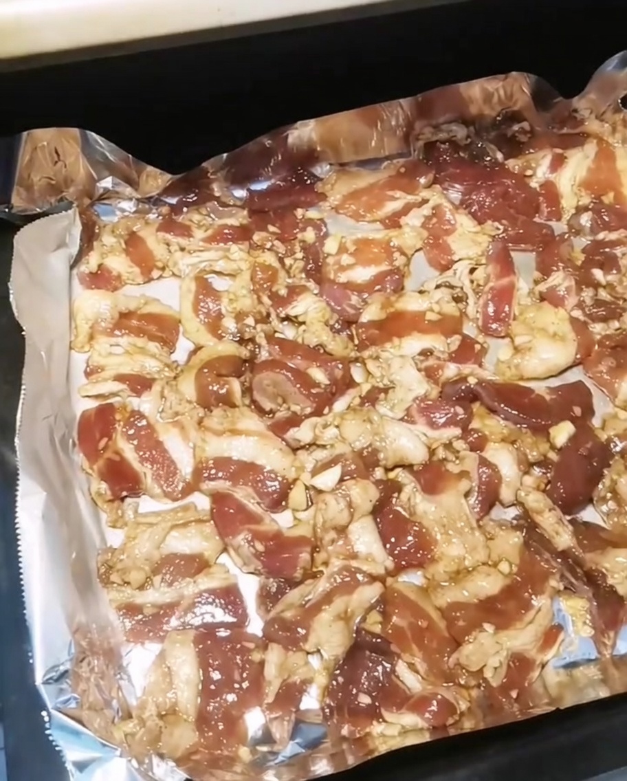 Una teglia piena di fette di pancetta condita inserita in un forno caldo.